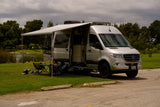 Family enjoys their silver Mercedes Sprinter rv rental, complete with an extended awning setup beside a scenic lake.