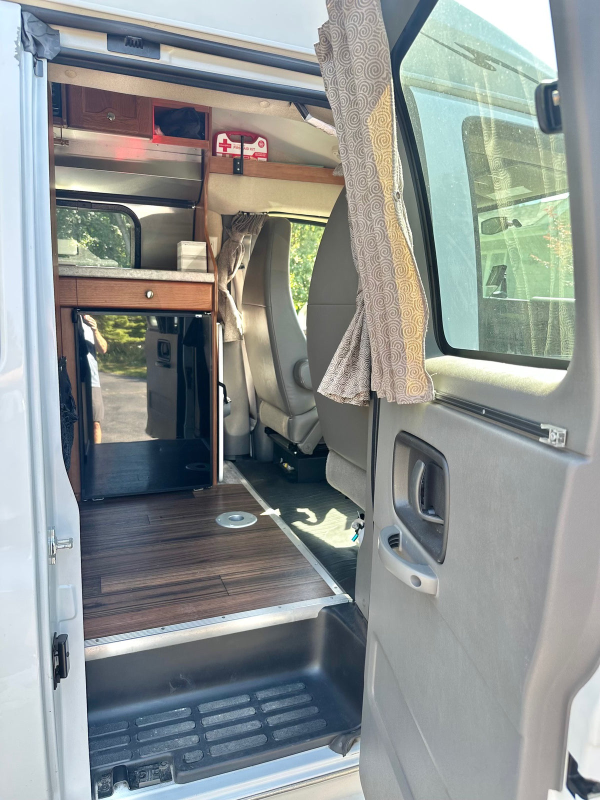 Inside an RV rental: view from the side door showing a compact kitchen, wood flooring, and seating area with privacy curtains. — photo 11