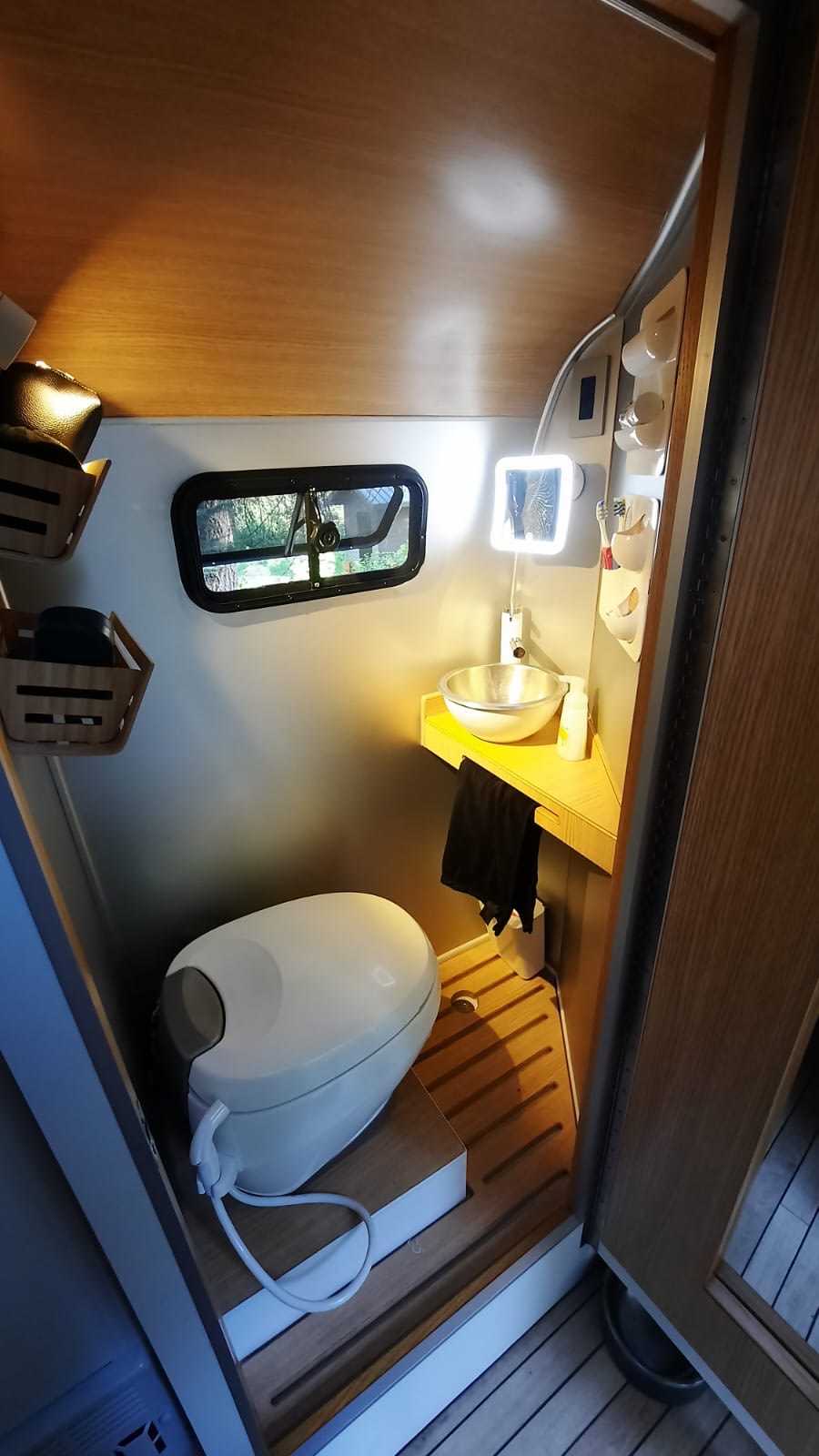 Inside an RV rental: a compact and well-equipped bathroom with a toilet, corner sink, mirror, and storage solutions. — photo 7