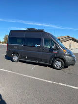 Dark grey Ram ProMaster RV rental parked outdoors under a clear blue sky. Ready for your next adventure.