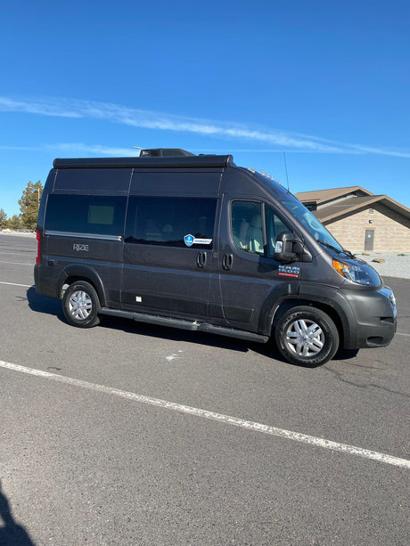Dark grey Ram ProMaster RV rental parked outdoors under a clear blue sky. Ready for your next adventure.
