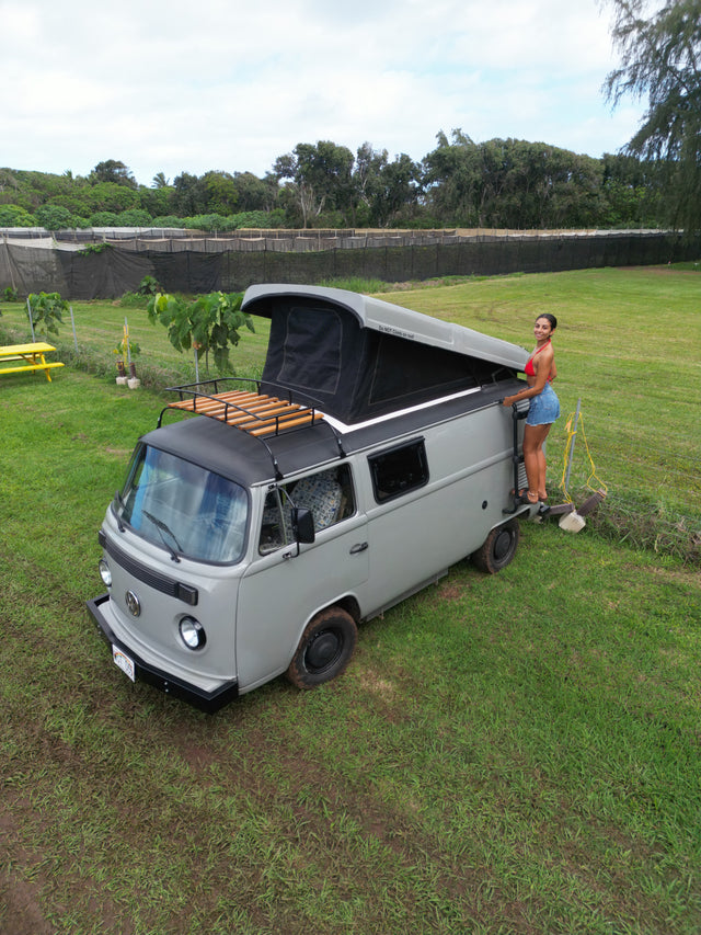 Woman with a vintage pop-top RV rental in a grassy field, ready for outdoor adventures.