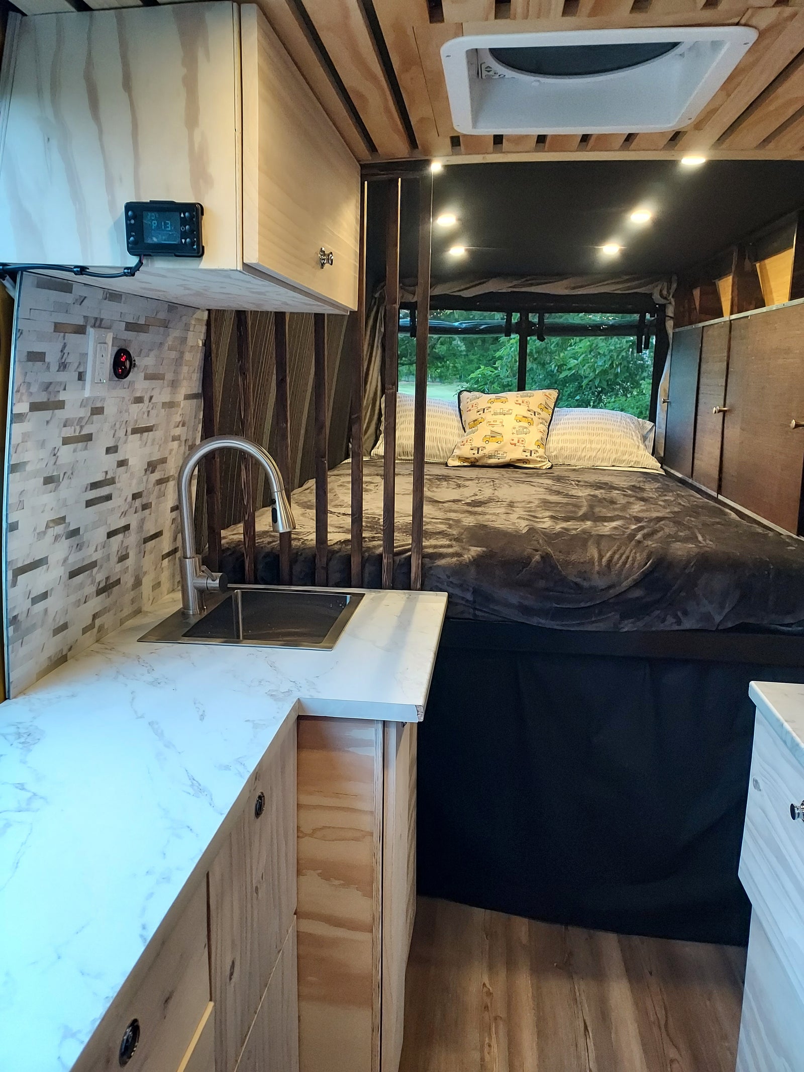 Cozy RV rental interior with a bed, compact kitchen with sink, wood paneling, string lights, and a window view.