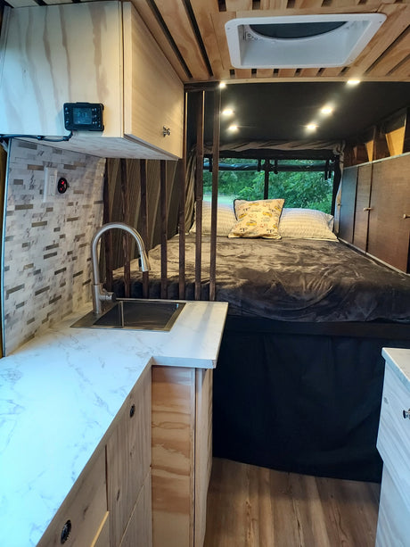 Cozy RV rental interior with a bed, compact kitchen with sink, wood paneling, string lights, and a window view.
