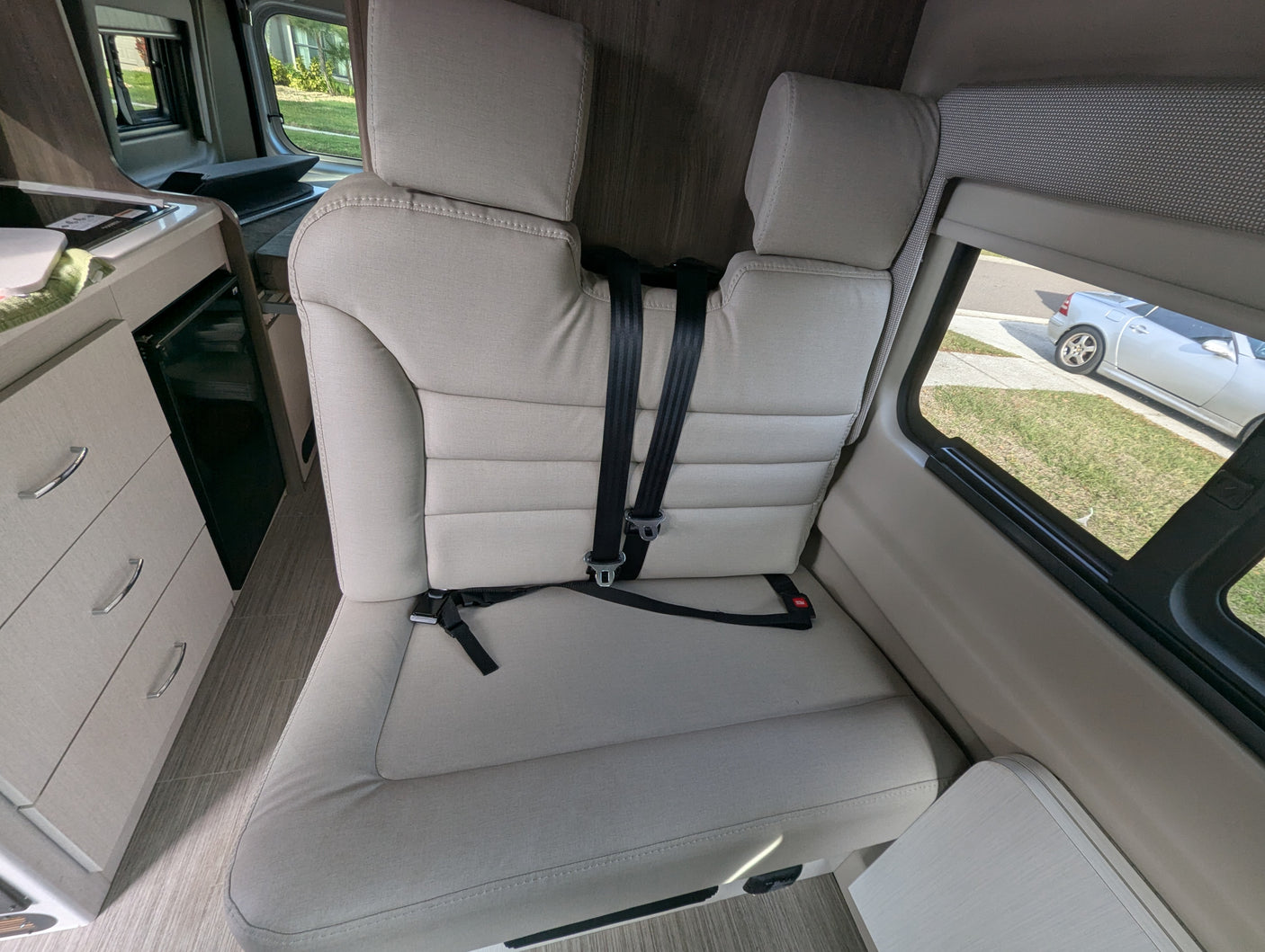 RV rental interior showing a comfortable bench seat with seat belts, a compact kitchenette, and a window view.