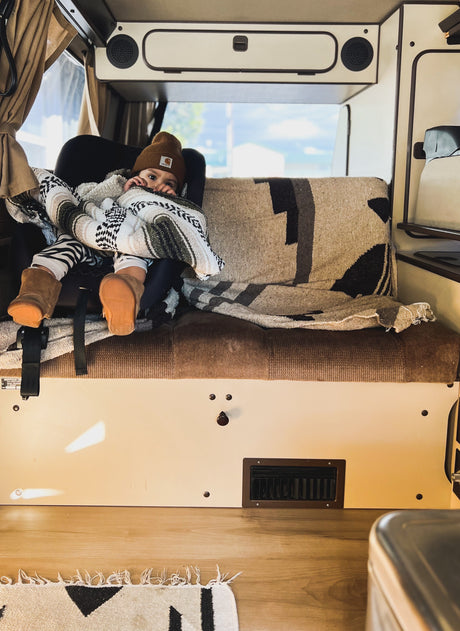 Cozy child in a Carhartt beanie, snuggled in a blanket inside an RV rental. Ready for a family road trip adventure!
