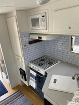 Stylish RV rental kitchen with white subway tile backsplash, compact stove, microwave, sink, and blue lower cabinets.