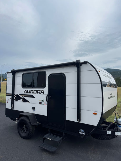White and black Forest River Aurora teardrop RV rental, showing its side profile with windows, door, awning, and rugged tires.