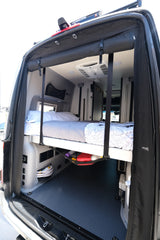 Rear view of an RV rental's clever interior, showcasing a raised bed, under-bed storage, and air conditioning unit.