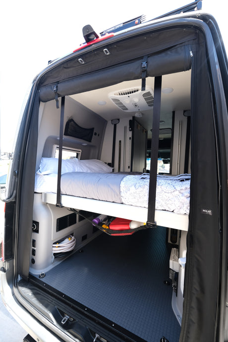 Rear view of an RV rental's clever interior, showcasing a raised bed, under-bed storage, and air conditioning unit.