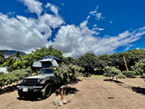 Explore with an RV rental! This Jeep with a rooftop tent is ready for camping at site #3, surrounded by lush trees.