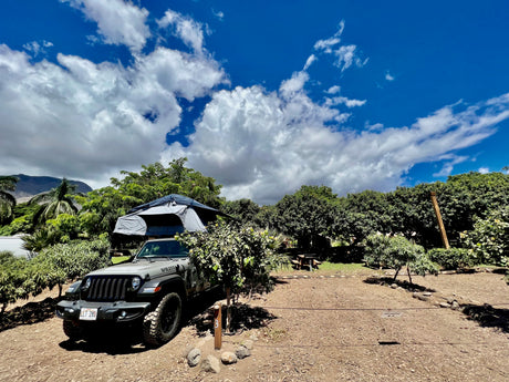 Explore with an RV rental! This Jeep with a rooftop tent is ready for camping at site #3, surrounded by lush trees.