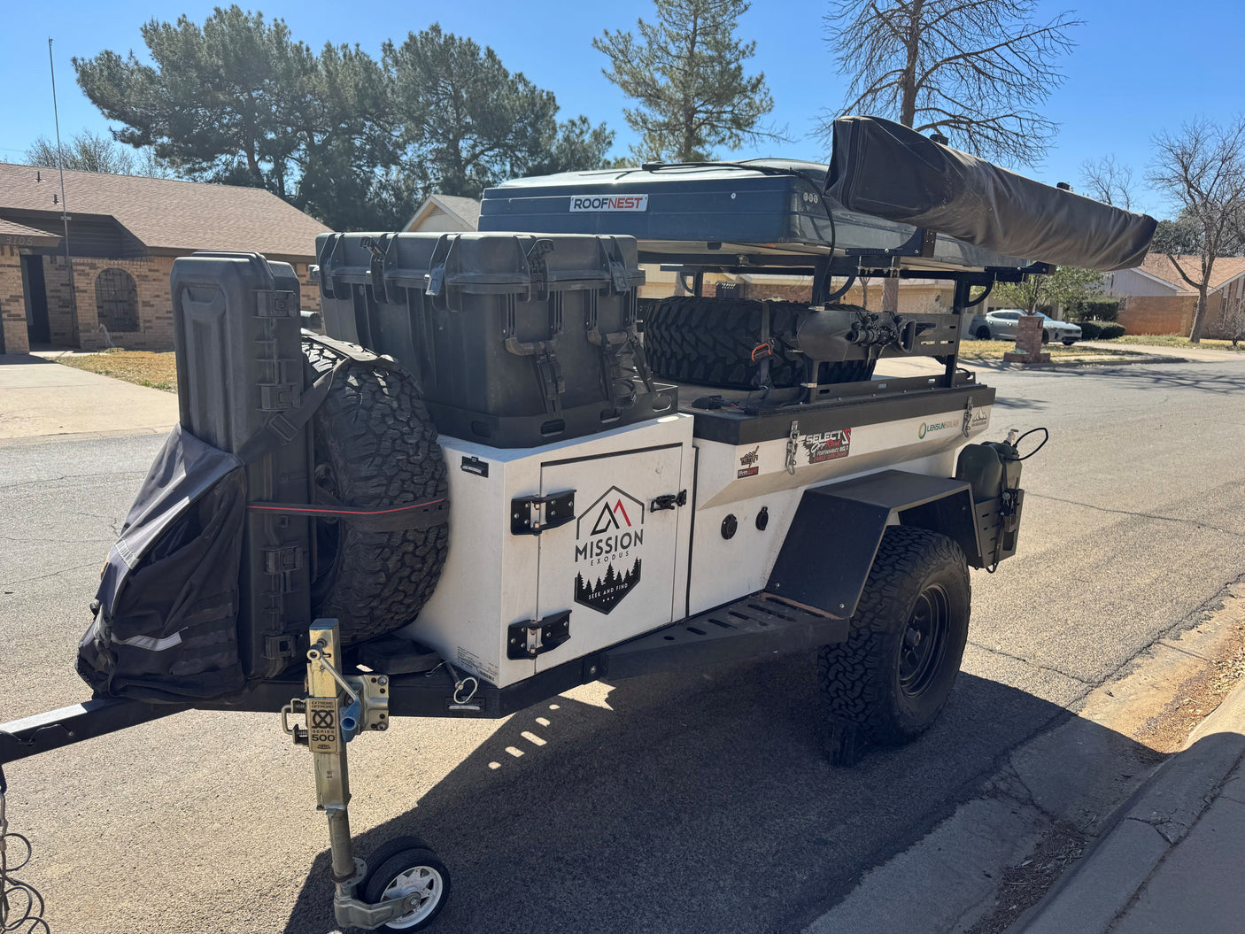 A sturdy white overland camper trailer with a dark blue rooftop tent and gear, parked on a street, perfect for an RV rental adventure.