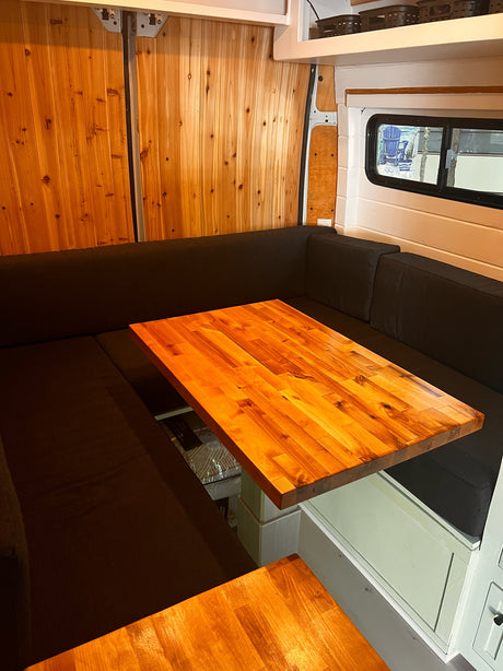 RV rental interior features a U-shaped dark cushioned seating area with a rich wooden table, ideal for dining.