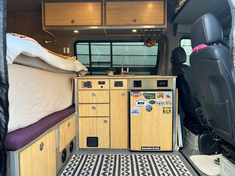 RV rental interior: cozy bed, custom bamboo kitchen with sink & fridge, plus front seats. Ideal for van life adventures! — photo 8