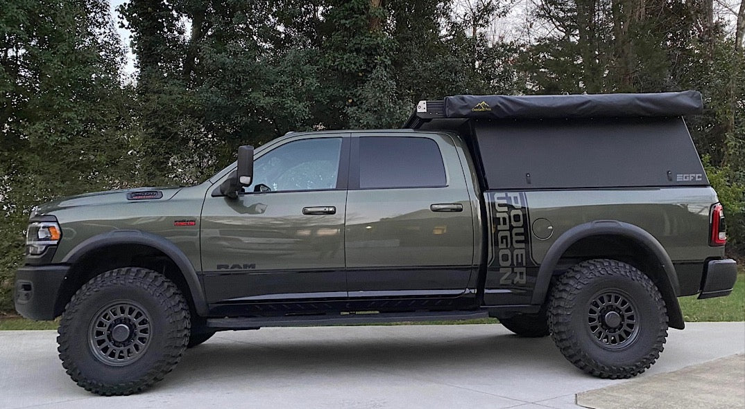 Olive green Ram Power Wagon with a truck camper and awning, an ideal RV rental for overlanding adventures.