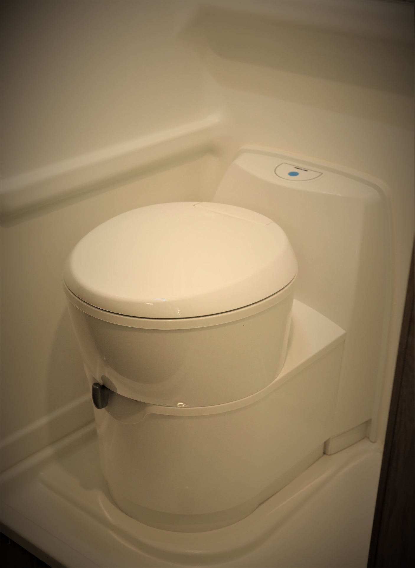 Interior view of a clean, modern, compact RV rental toilet with a blue indicator light.