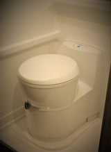 Interior view of a clean, modern, compact RV rental toilet with a blue indicator light.