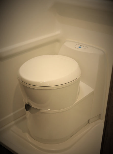 Interior view of a clean, modern, compact RV rental toilet with a blue indicator light.