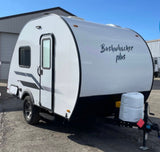 A Bushwhacker Plus teardrop travel trailer, a compact RV rental. Features a white body, black bottom, and all-terrain tires.
