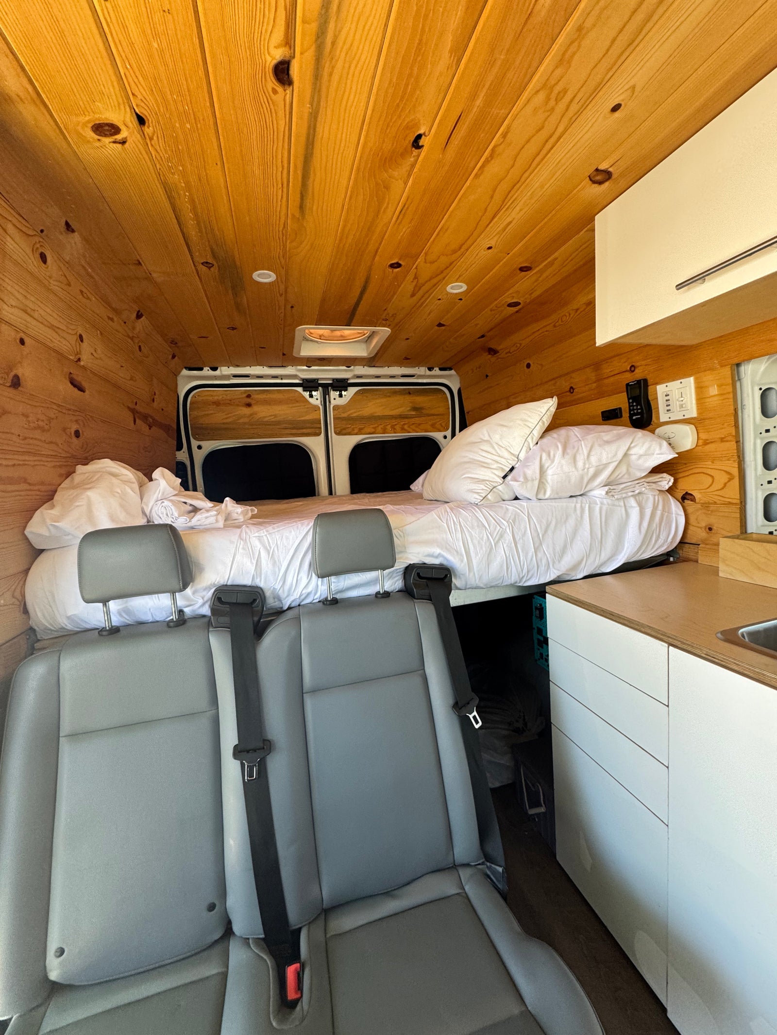 Interior of a cozy RV rental: wood-paneled walls, bed, kitchenette, and passenger seats.