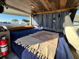 Cozy RV rental interior with a comfortable bed, fan, and scenic view. A fire extinguisher is visible for safety.