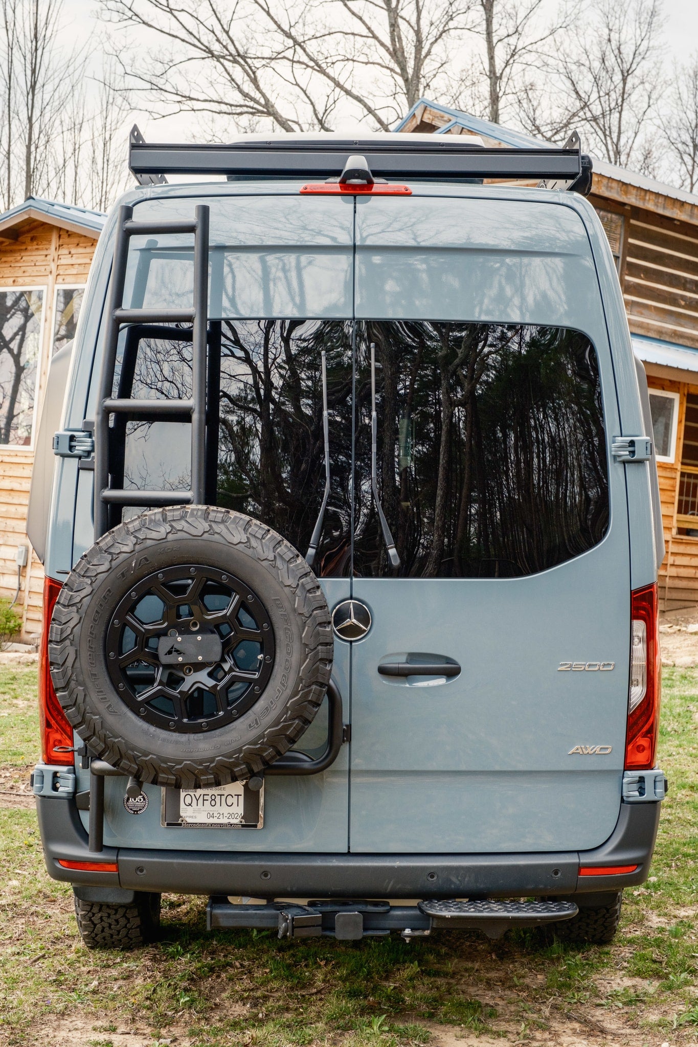 Rear of an AWD Mercedes Sprinter camper van, ideal for rv rental adventures, featuring a ladder, spare tire, and roof rack. — photo 6
