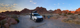Sunrise at a desert campsite features an RV rental camper van parked amidst stunning red rock formations.