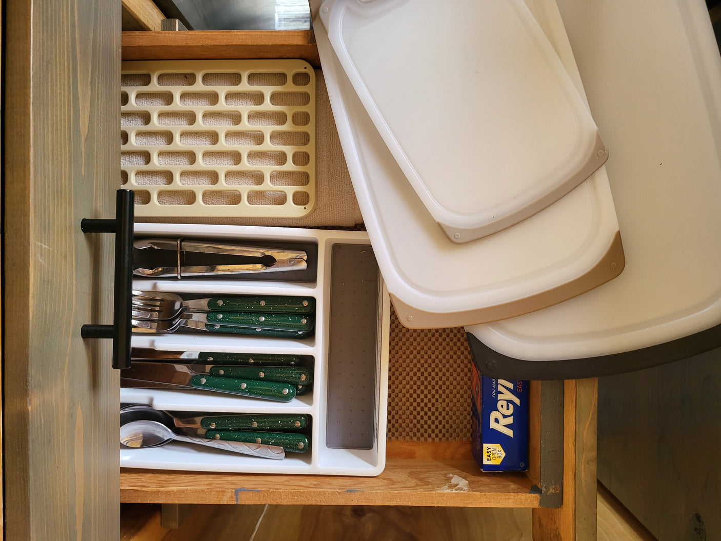 This RV rental's kitchen drawer is neatly organized with green-handled utensils, stacked cutting boards, and foil, ready for your trip.