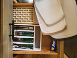 This RV rental's kitchen drawer is neatly organized with green-handled utensils, stacked cutting boards, and foil, ready for your trip.
