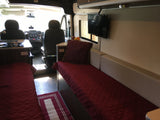 Interior of an RV rental features a compact kitchen, sleeping area, bench seating, and a TV, looking towards the cab.
