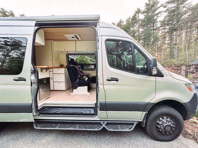 Stylish van conversion rv rental with open side door revealing a light-colored exterior and a custom interior with kitchenette & car seat.