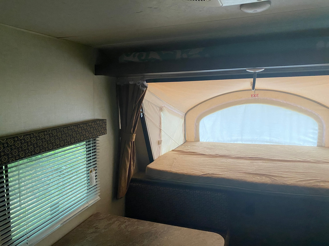 Interior of an RV rental: a cozy expandable bed with 'EXIT' sign, window with blinds, and a table. — photo 5