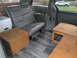 RV rental minivan interior showing a rear seat, white cooler, and wooden storage on a gray plank floor.