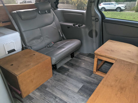 RV rental minivan interior showing a rear seat, white cooler, and wooden storage on a gray plank floor.
