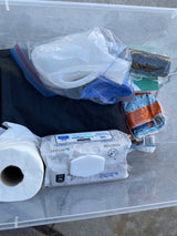 RV rental hygiene kit: Portable toilet, Kirkland wipes, toilet paper, and waste bags, all in a clear storage bin for camping.