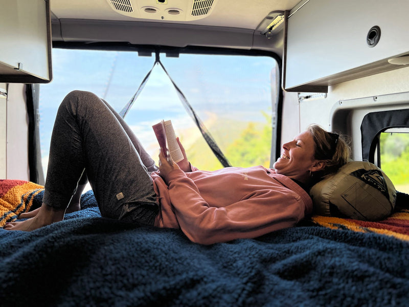  and wall-mounted solar controls.|A woman smiles while relaxing and reading a book inside a cozy RV rental — photo 7
