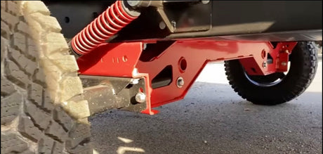 Detailed view of an off-road trailer's red heavy-duty suspension and rugged tires, ready for RV rental adventures.