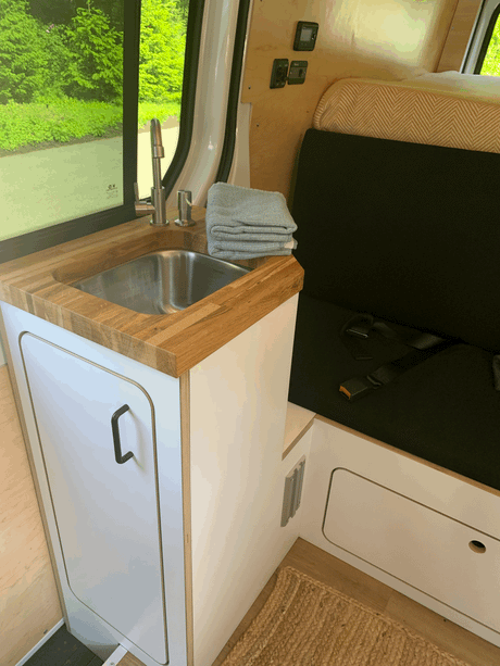 Clean RV rental interior featuring a wooden-counter sink, comfortable bench seating, & controls.