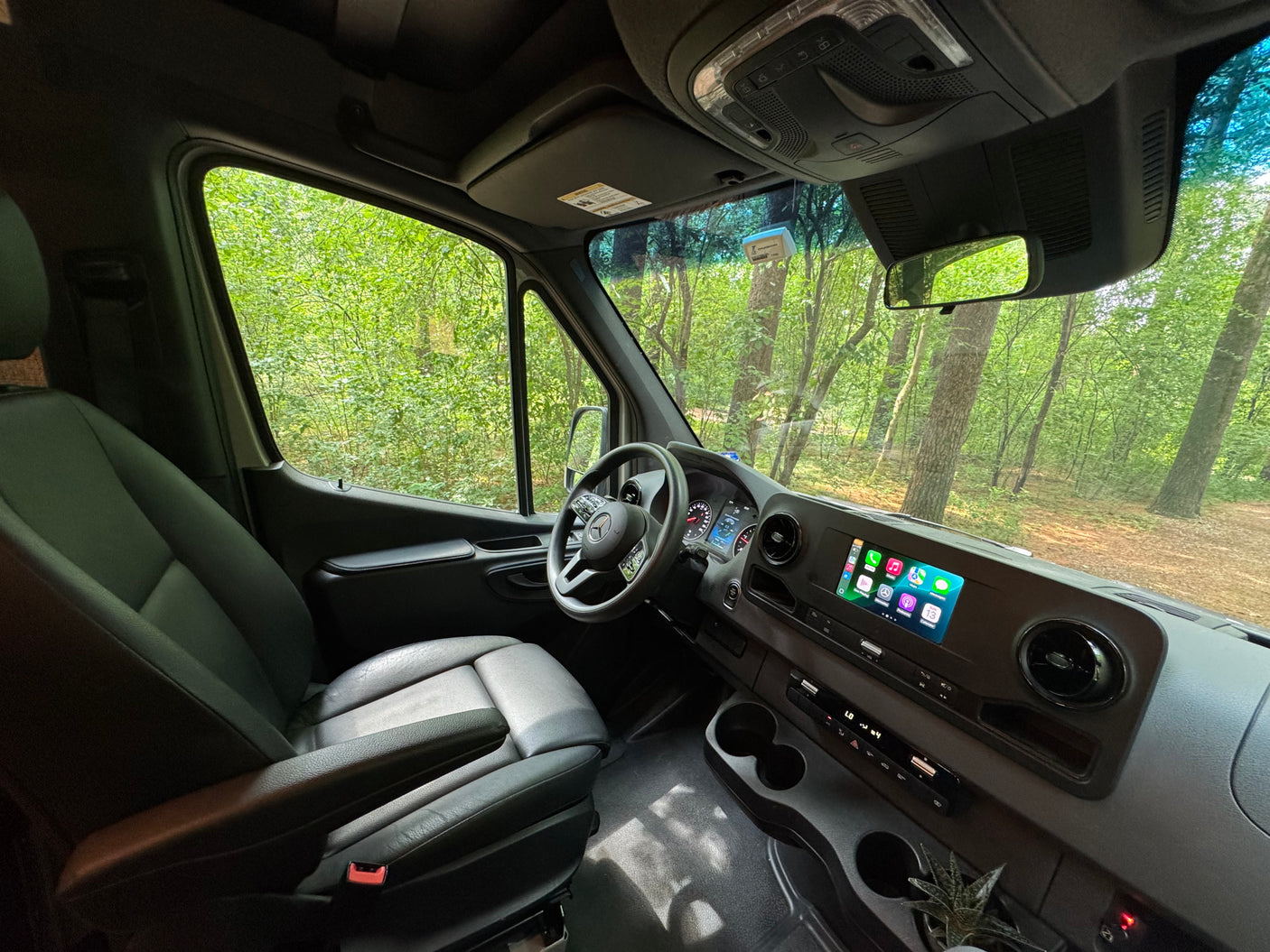 RV rental interior: modern van cockpit, infotainment screen, comfy seat, and lush forest outside.