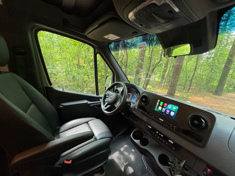 RV rental interior: modern van cockpit, infotainment screen, comfy seat, and lush forest outside.