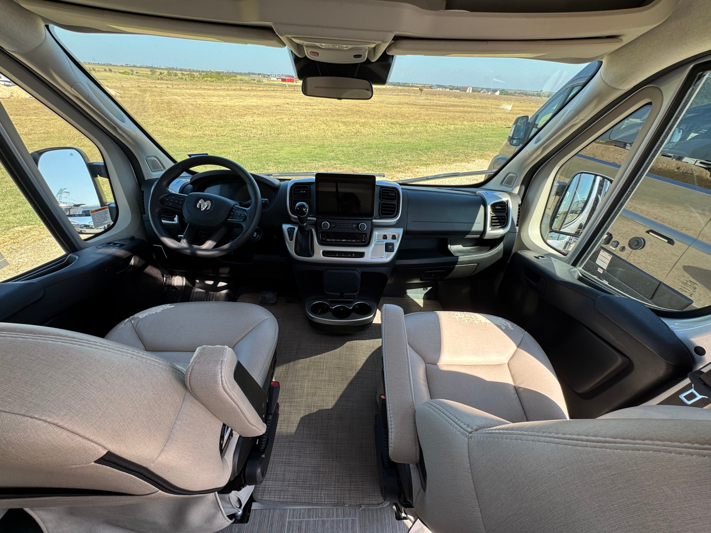 Inside an RV rental, the spacious driver's area has beige seats, a modern dashboard, and clear views of the open field. — photo 4