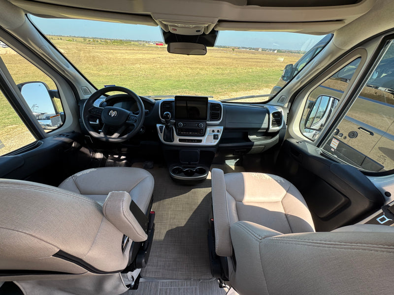 Inside an RV rental, the spacious driver's area has beige seats, a modern dashboard, and clear views of the open field. — photo 4