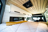 Explore this modern RV rental interior, featuring a large bed, sleek white cabinets, wood ceiling, and kitchenette.