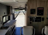 This RV rental's camper van interior features a compact kitchenette on the left and control panels on the right, with open rear doors.