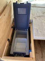 This RV rental features an open portable fridge/freezer, built into a wooden cabinet, offering convenient cold storage for travelers.