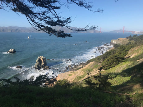 Stunning Pacific Ocean view of the Golden Gate Bridge from coastal cliffs, perfect for an RV rental road trip. Spot a sailboat & lighthouse!