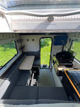 Bright rv rental interior features a U-shaped dining area, compact kitchen with stove, and outdoor access to green space.