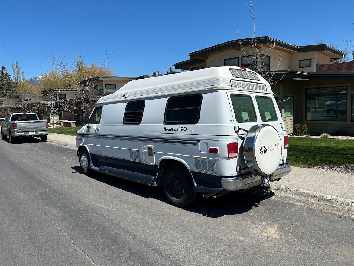White Roadtrek 190 Popular camper van RV rental parked on a sunny street, residential background, mountains beyond.
