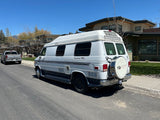 White Roadtrek 190 Popular camper van RV rental parked on a sunny street, residential background, mountains beyond.